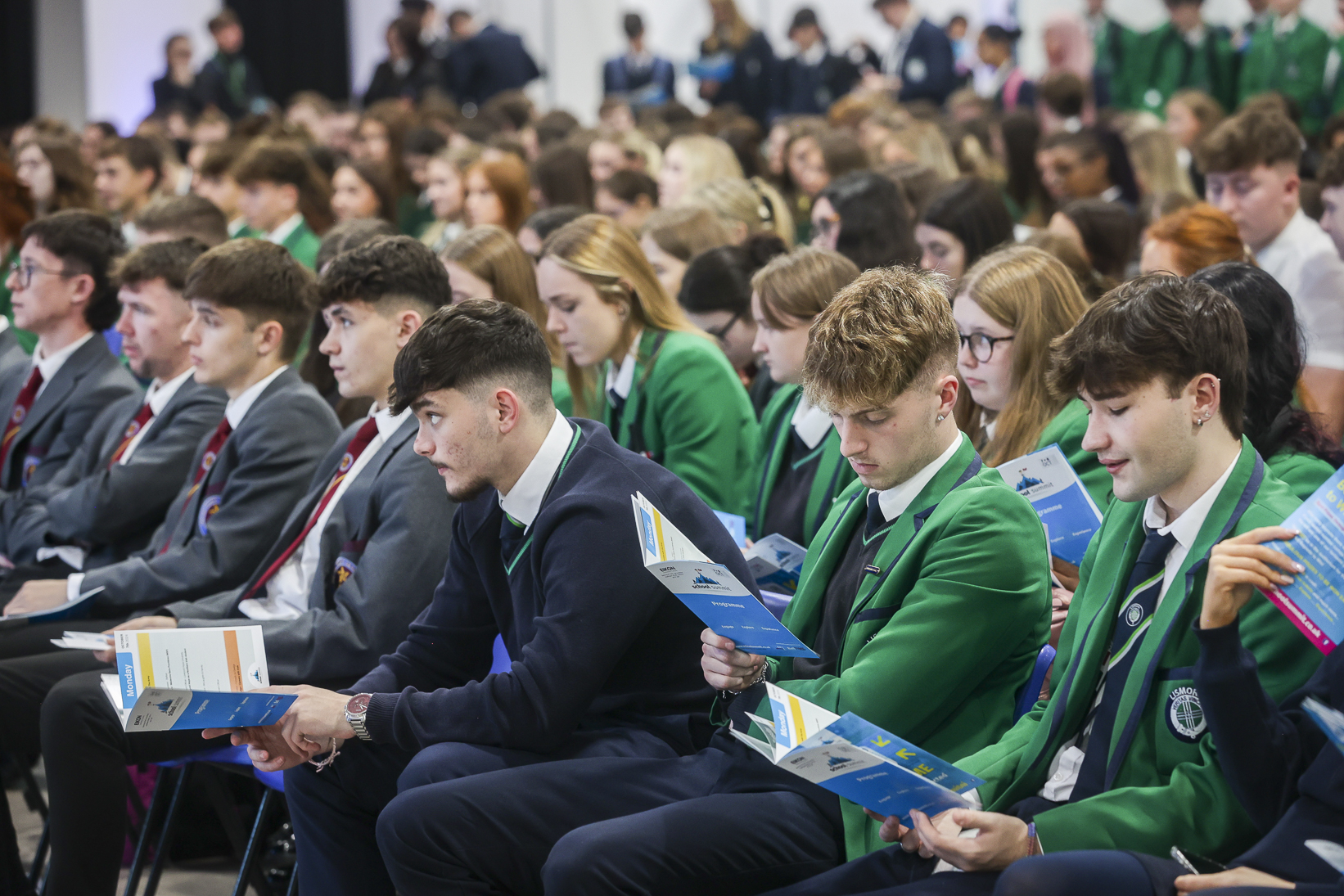 Packed auditorium of secondary-school pupils in blazers seated for the School Summit Northern Ireland main stage, 2024.
