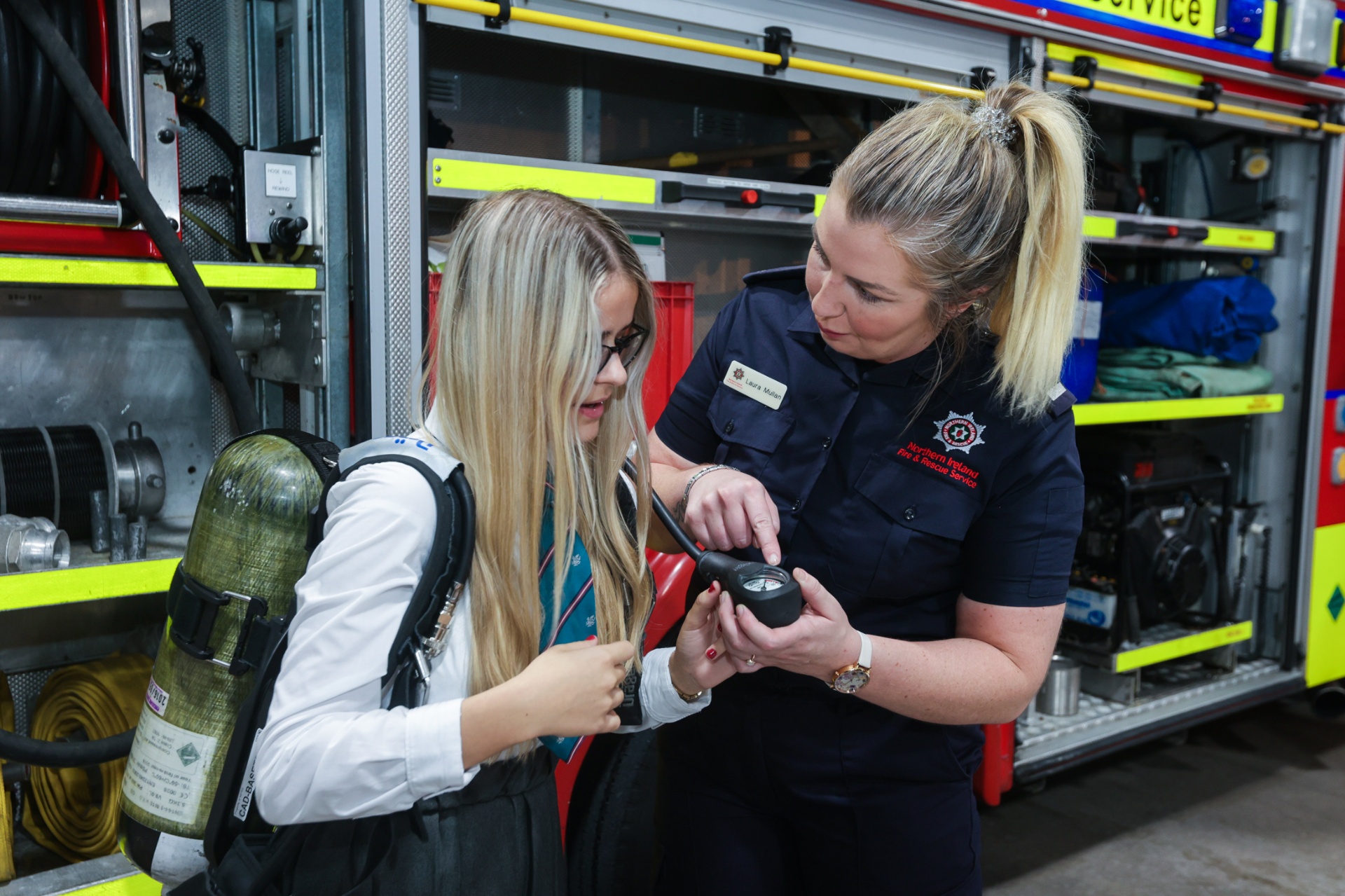 A female Northern Ireland Fire & Rescue Service firefighter demonstrating breathing apparatus to a pupil at School Summit NI, 2022.