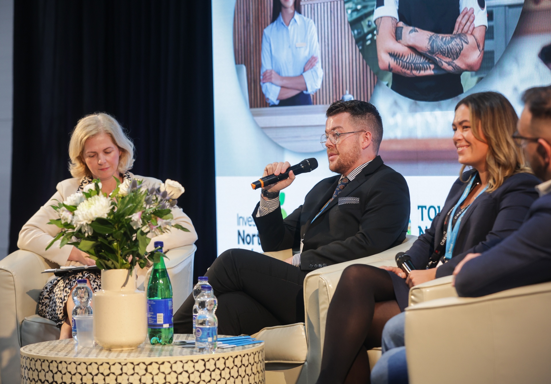 Panel of industry speakers seated on the School Summit Northern Ireland main stage, with the discussion projected on the screen behind them, 2023.