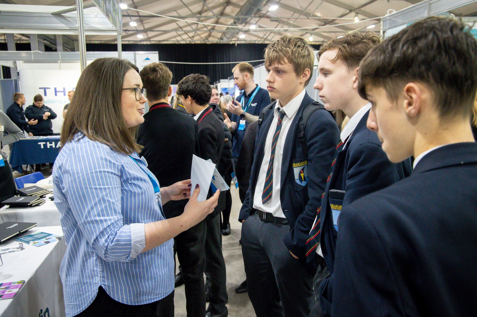 Translink staff in high-visibility uniforms speaking with pupils at their ‘ICYMI’ branded exhibitor stand at School Summit Northern Ireland, 2025.
